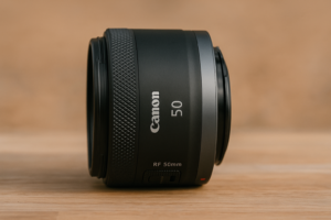 Canon RF 50mm f/1.8 STM Objektiv liegend auf einer Holzfläche mit unscharfem beigefarbenem Hintergrund, seitlich fotografiert