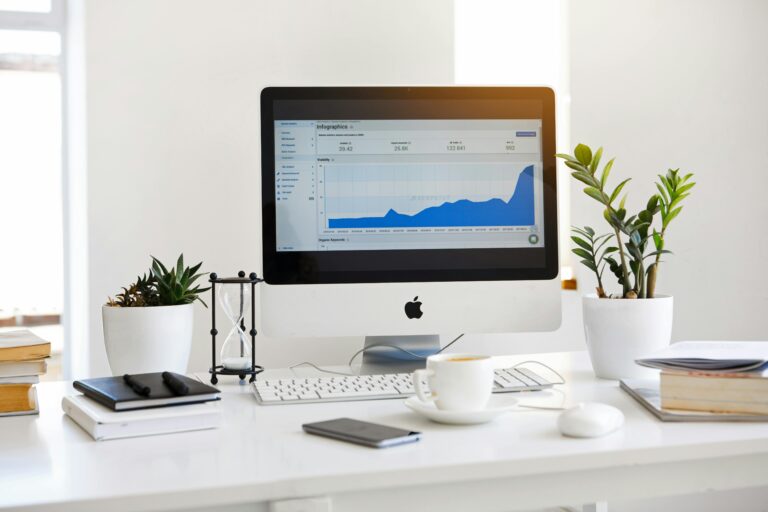 iMac auf einem weißen Schreibtisch mit Pflanzen, Büchern und Kaffee – Technik dezent ins Interior integriert